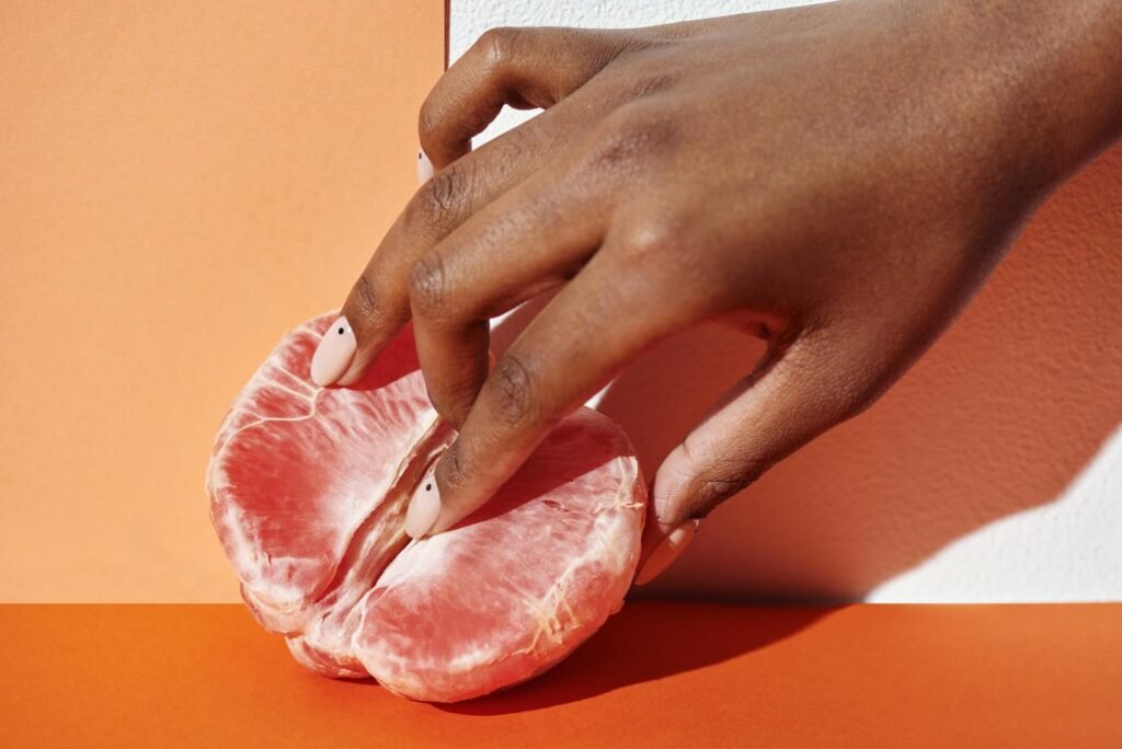 Close-up of a hand gently touching a grapefruit against an orange background, showcasing freshness and elegance.